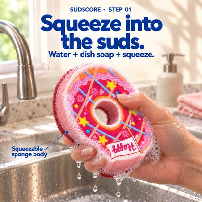 An adult hand gently squeezing the wet Pink Ring Donut with normal dish-soap lather above a kitchen sink.